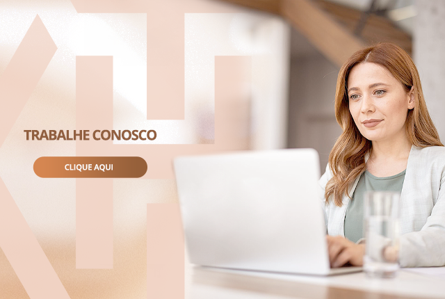 Uma mulher está sentada em uma mesa usando um laptop.