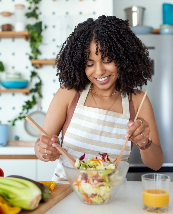 Uma mulher está misturando uma salada em uma tigela com colheres de pau.