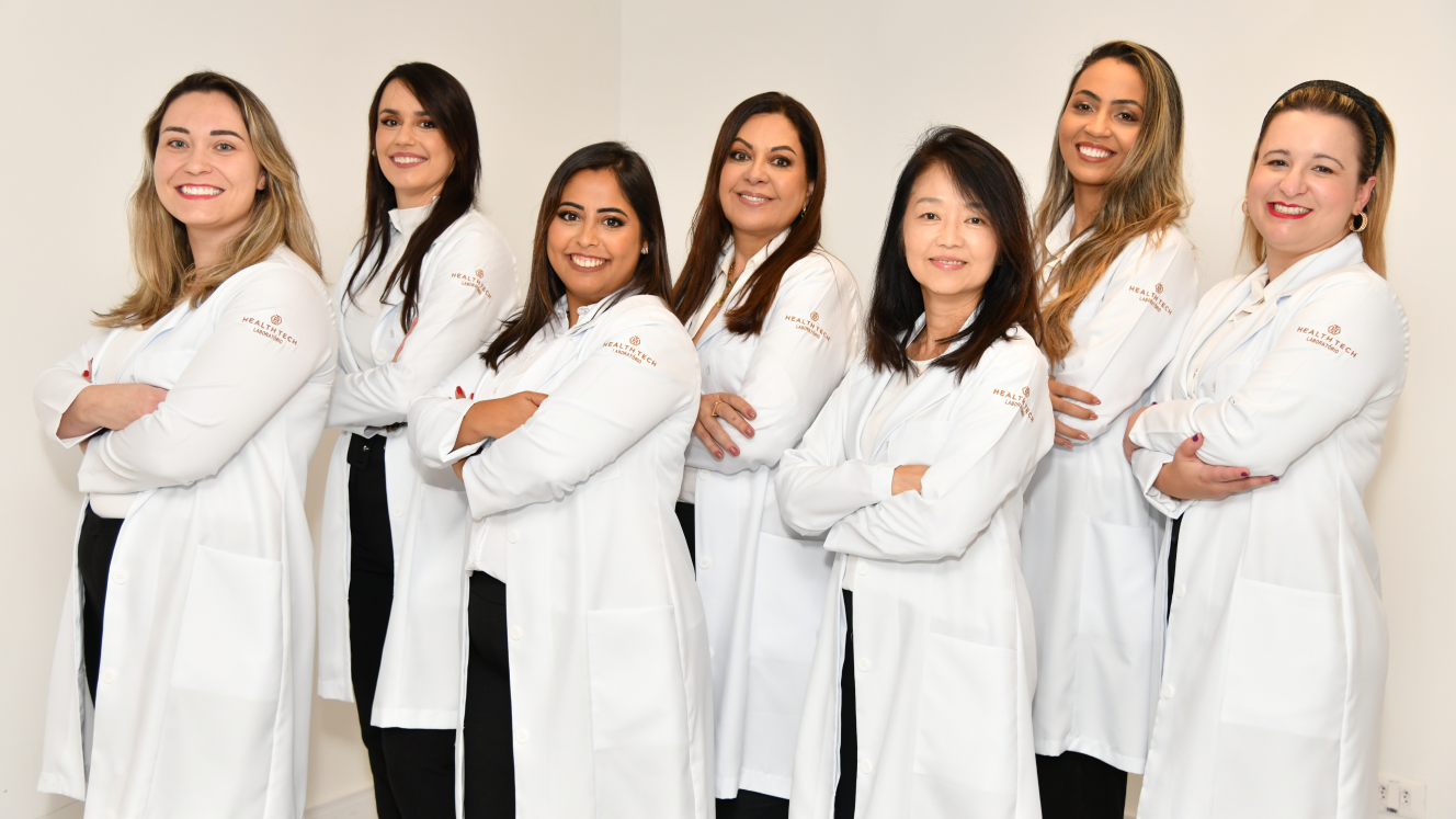 Um grupo de mulheres de jaleco branco estão posando para uma foto.